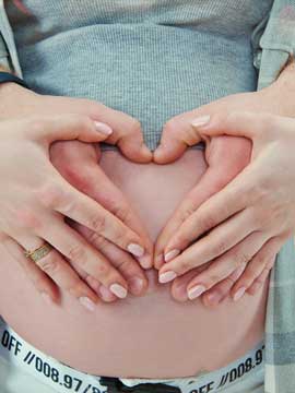 Schwangere hält Ihre und die Hände einer zweiten Person auf Ihrem Bauch nackten zu einem Herzen.