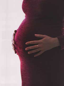 Schwangere Frau in roten Kleid hält ihren Bauch.
